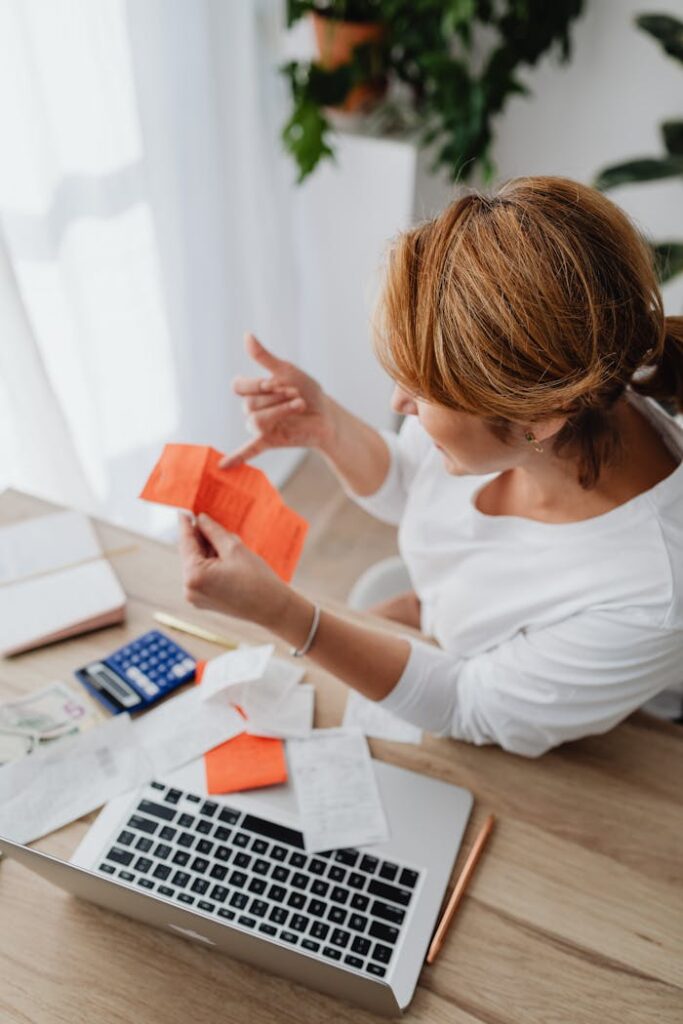 Top view of a woman managing finances on a laptop surrounded by receipts and calculator.